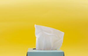 An image of a blue box of white tissues against a yellow background.