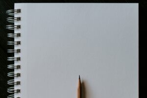 A sharpened pencil rests on the blank white page of a spiral notebook.